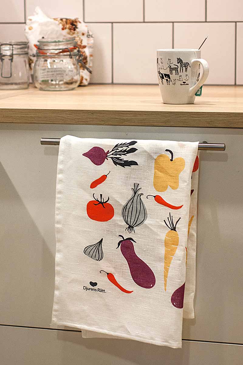Vit kökshandduk med illustration av olika grönsaker och Djurens Rätts logga